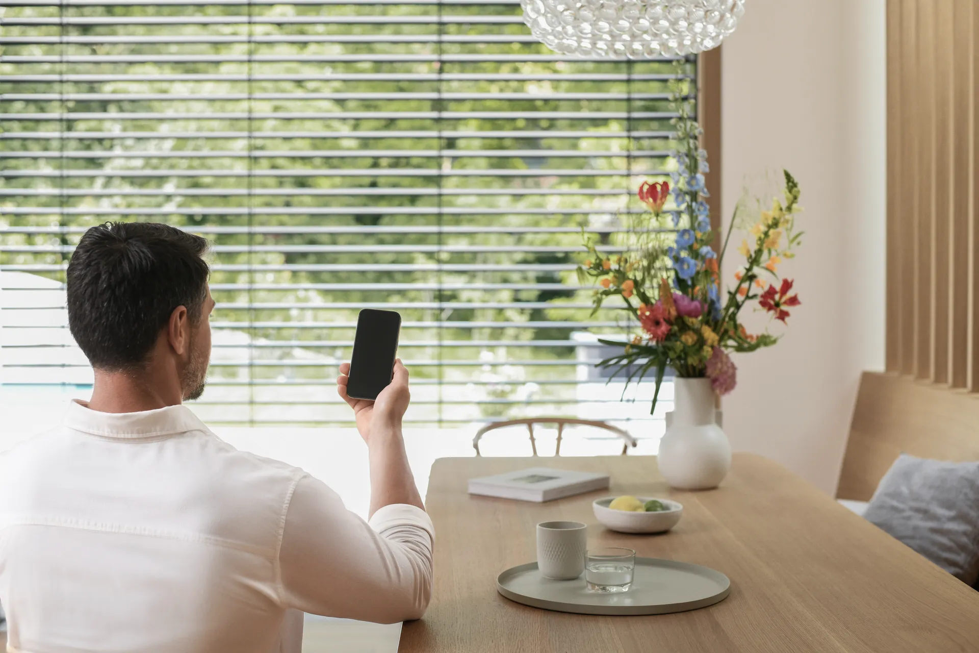 Offenes Fenster mit Insektenschutz im Schlafzimmer Ein Mann stellt seinen Sonnenschutz per Smartphone ein